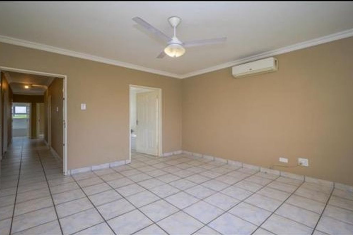 Spacious living area featuring neutral wall tones, tiled flooring, a ceiling fan, and a wall-mounted air conditioning unit.