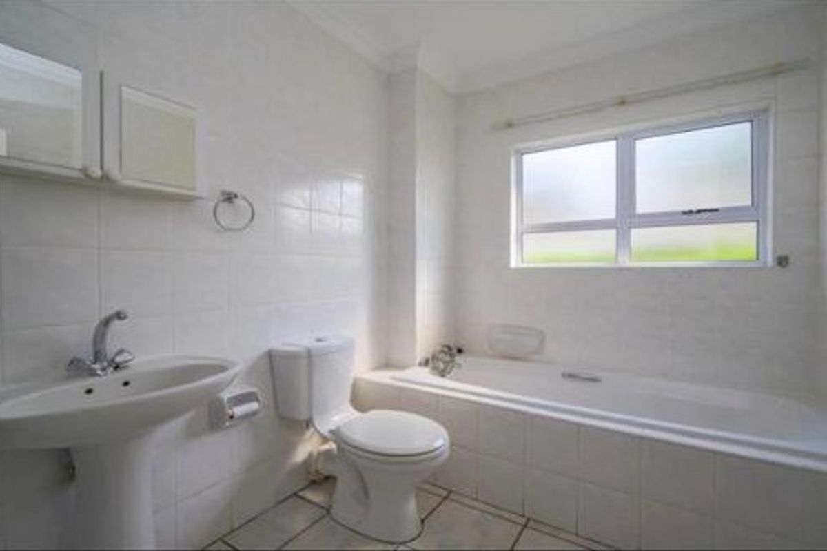 A functional bathroom featuring a pedestal sink, a built-in bathtub, and a standard toilet, finished with white wall tiles and tiled flooring.