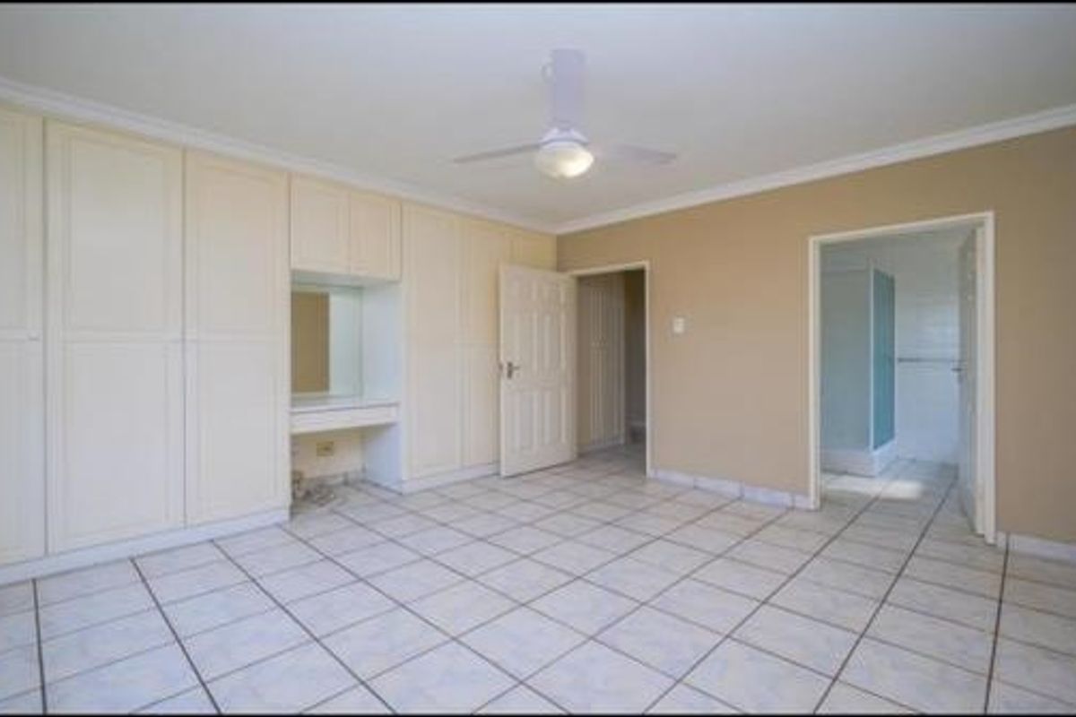 Spacious bedroom featuring extensive built-in cabinetry with a vanity area, tiled flooring, ceiling fan, and direct access to an en-suite bathroom.