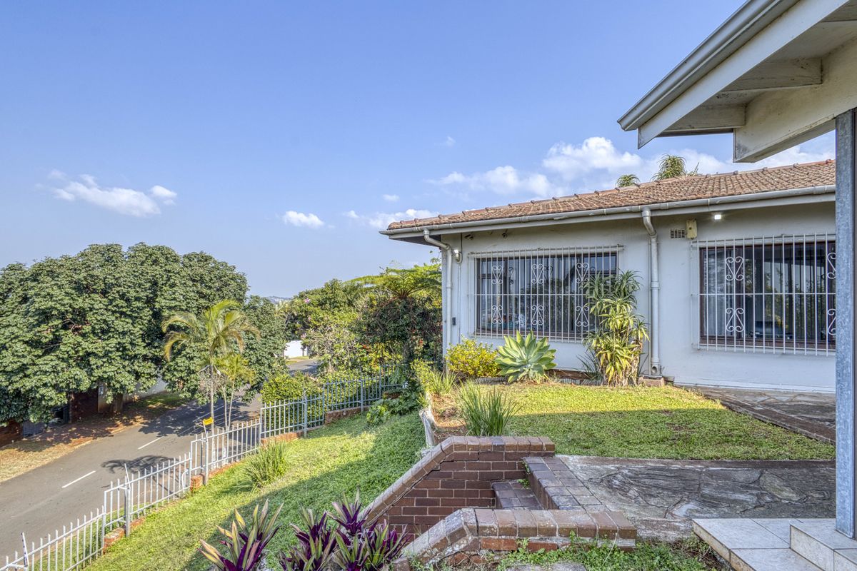 Exterior view of the property featuring a tiled roof, security bars on windows, and a landscaped garden area with brick retaining walls.