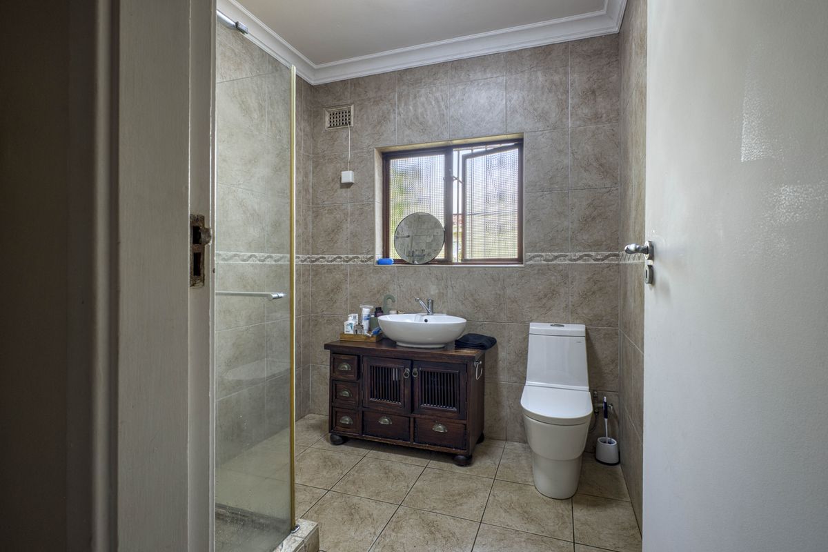 A functional bathroom featuring a glass-enclosed shower, a vessel sink vanity, and a modern toilet with neutral wall and floor tiling.