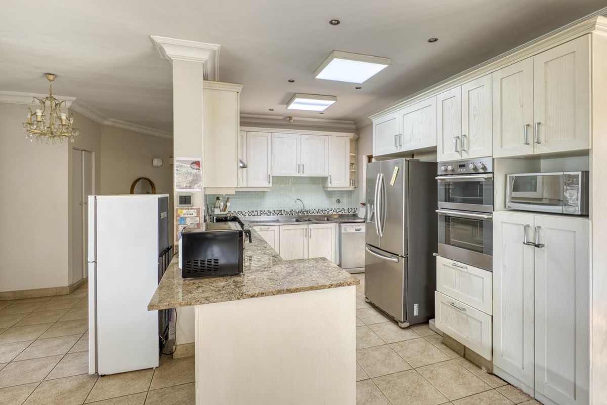 Spacious kitchen featuring light-toned cabinetry, granite countertops, built-in double ovens, and a breakfast bar, seamlessly flowing into the adjacent living area.
