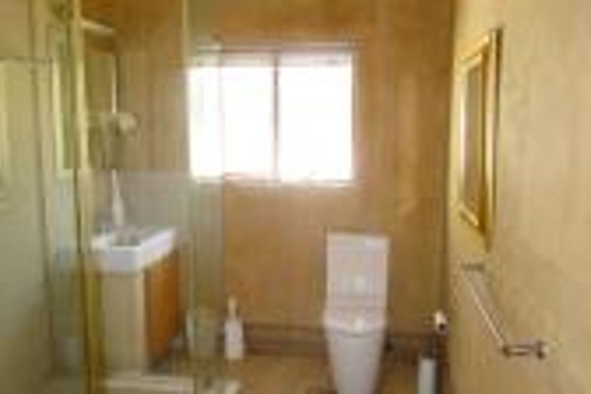 A functional bathroom featuring a glass shower enclosure, vanity basin, and toilet with neutral wall tiling.