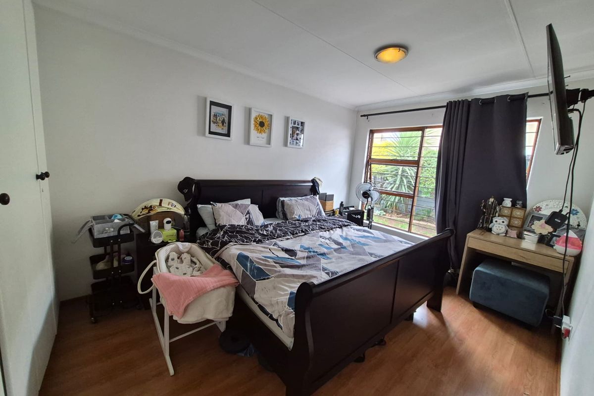 A functional bedroom featuring laminate flooring, a built-in cupboard, and a window with security bars, providing a comfortable and practical living space.