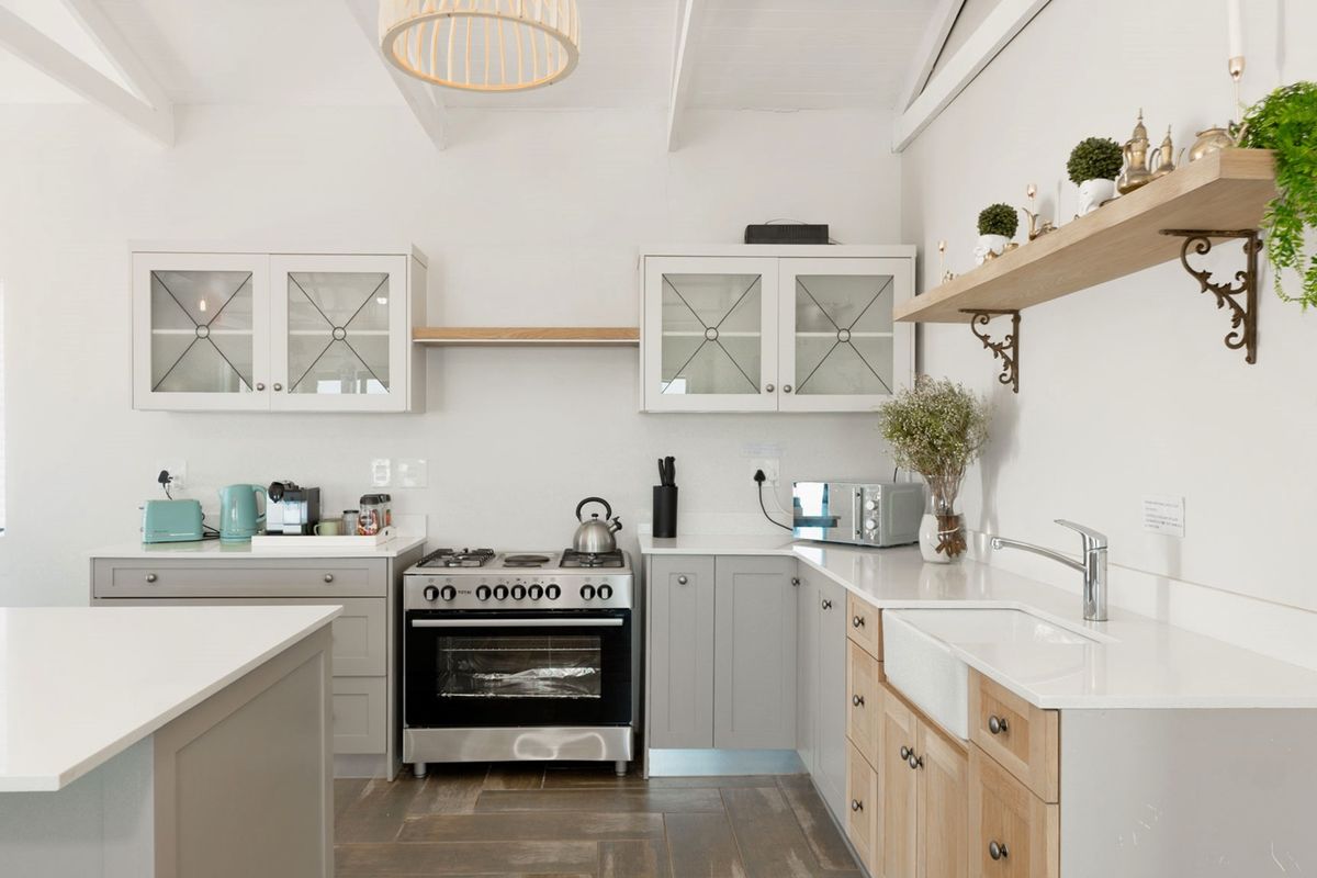 A bright, modern kitchen featuring shaker-style cabinetry, quartz countertops, an apron sink, and a gas stove under a vaulted ceiling.