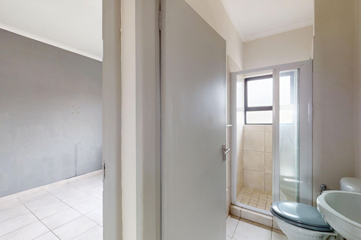 A functional bathroom featuring a shower enclosure, pedestal basin, and toilet, adjacent to an empty room with tiled flooring.