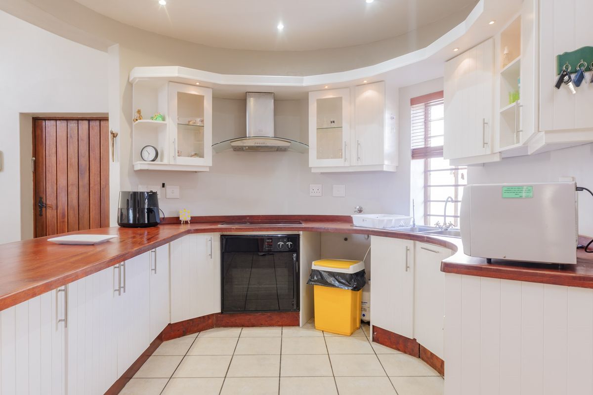 A functional kitchen featuring white cabinetry, warm wooden countertops, built-in oven and hob, and tiled flooring with recessed lighting.