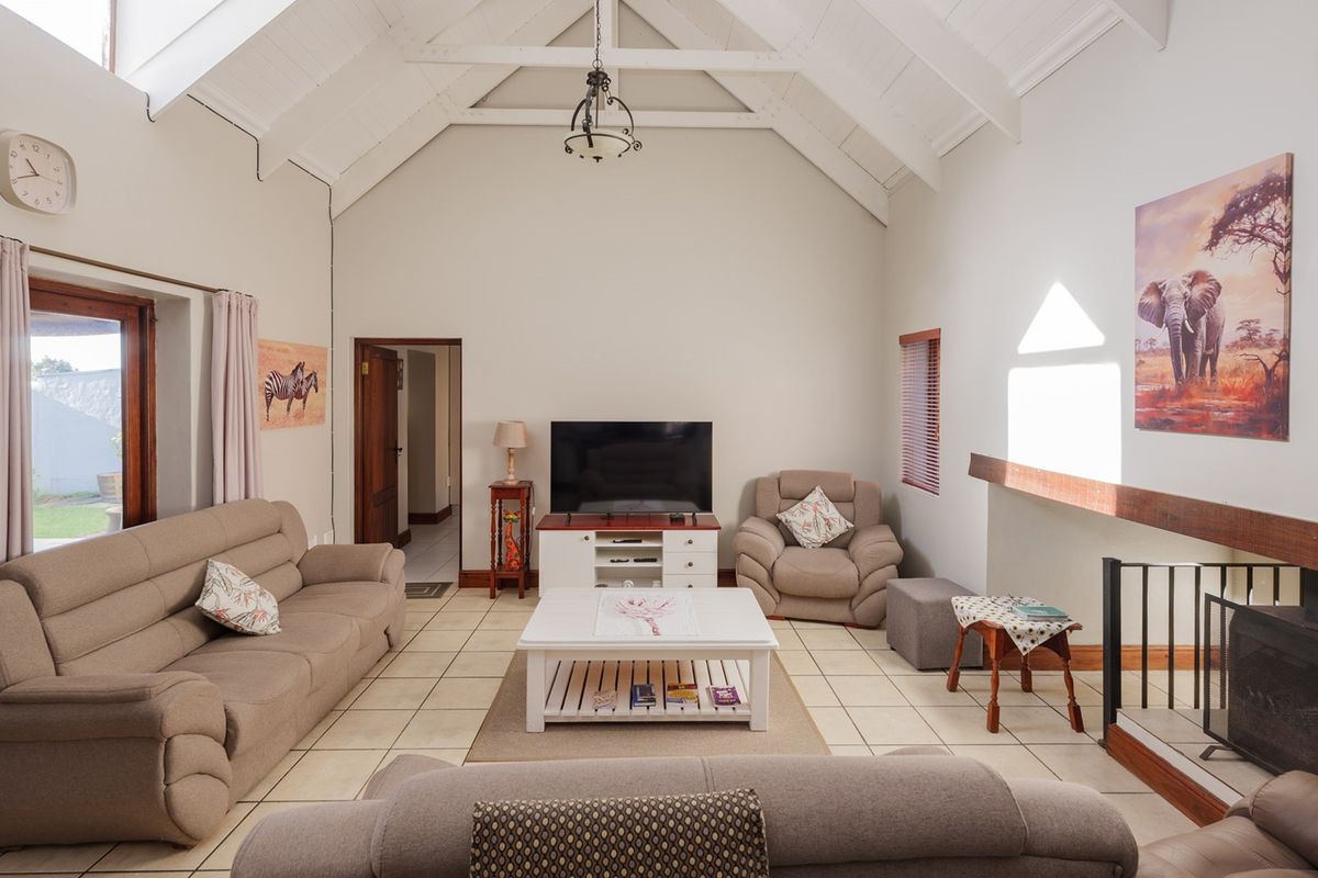 Spacious living room featuring a high vaulted ceiling with exposed beams, tiled flooring, and a fireplace with a timber mantelpiece.