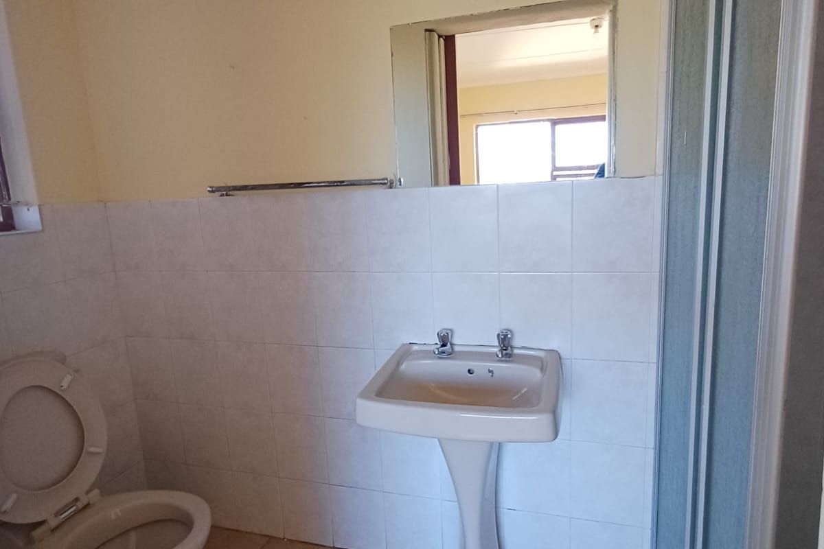 A functional bathroom featuring a pedestal washbasin, toilet, and shower enclosure with tiled finishes, offering a blank canvas for modernization.