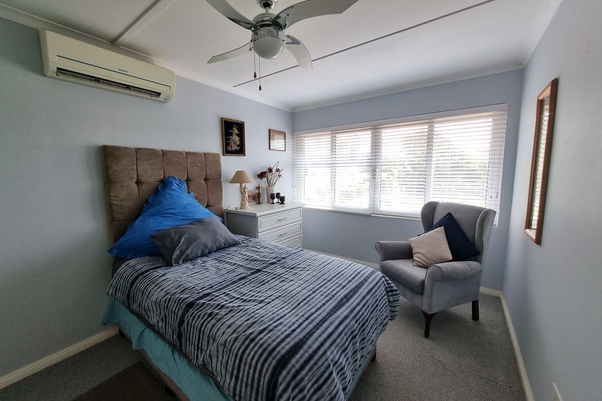 A well-lit bedroom featuring a ceiling fan, split-system air conditioning unit, and venetian blinds, providing a comfortable and functional living space.