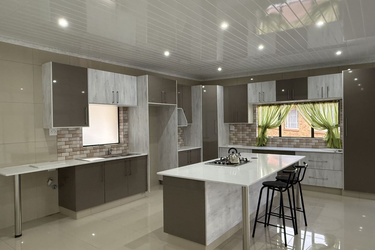 Modern kitchen featuring two-tone cabinetry, a central island with a gas hob, tiled splashbacks, and high-gloss floor tiles with recessed lighting.