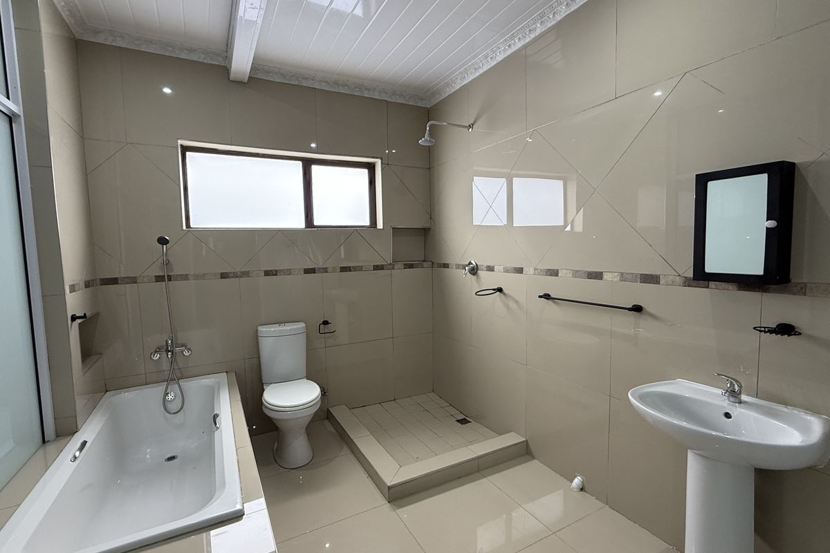 A spacious, fully tiled bathroom featuring a bathtub, a walk-in shower area, a pedestal basin, and a toilet.