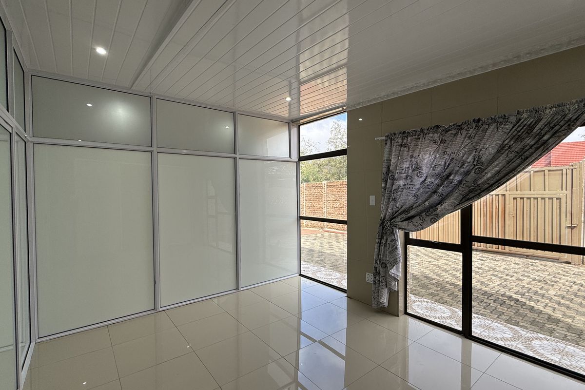 A bright, empty living area featuring polished tiled floors, modern glossy ceiling panels, and large aluminium-framed glass partitions providing natural light.
