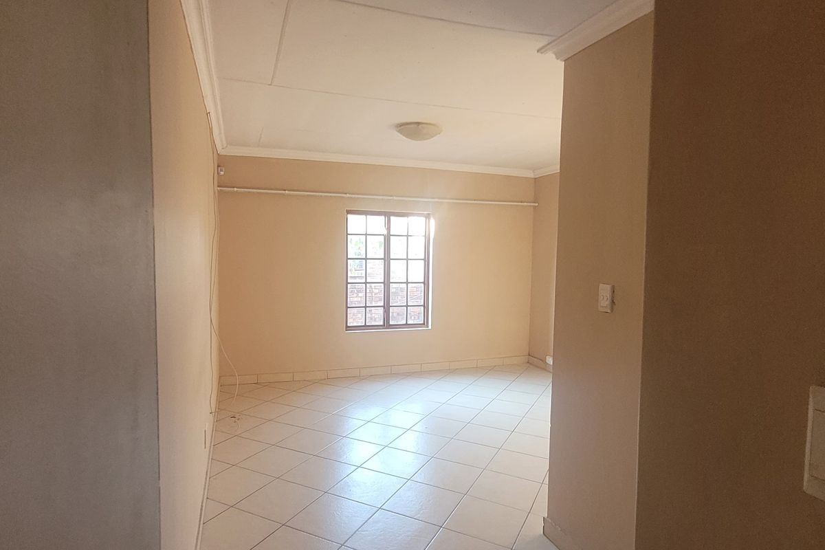 An empty living room featuring tiled flooring, coved ceilings, and a window with security bars, offering a neutral blank canvas for interior design.