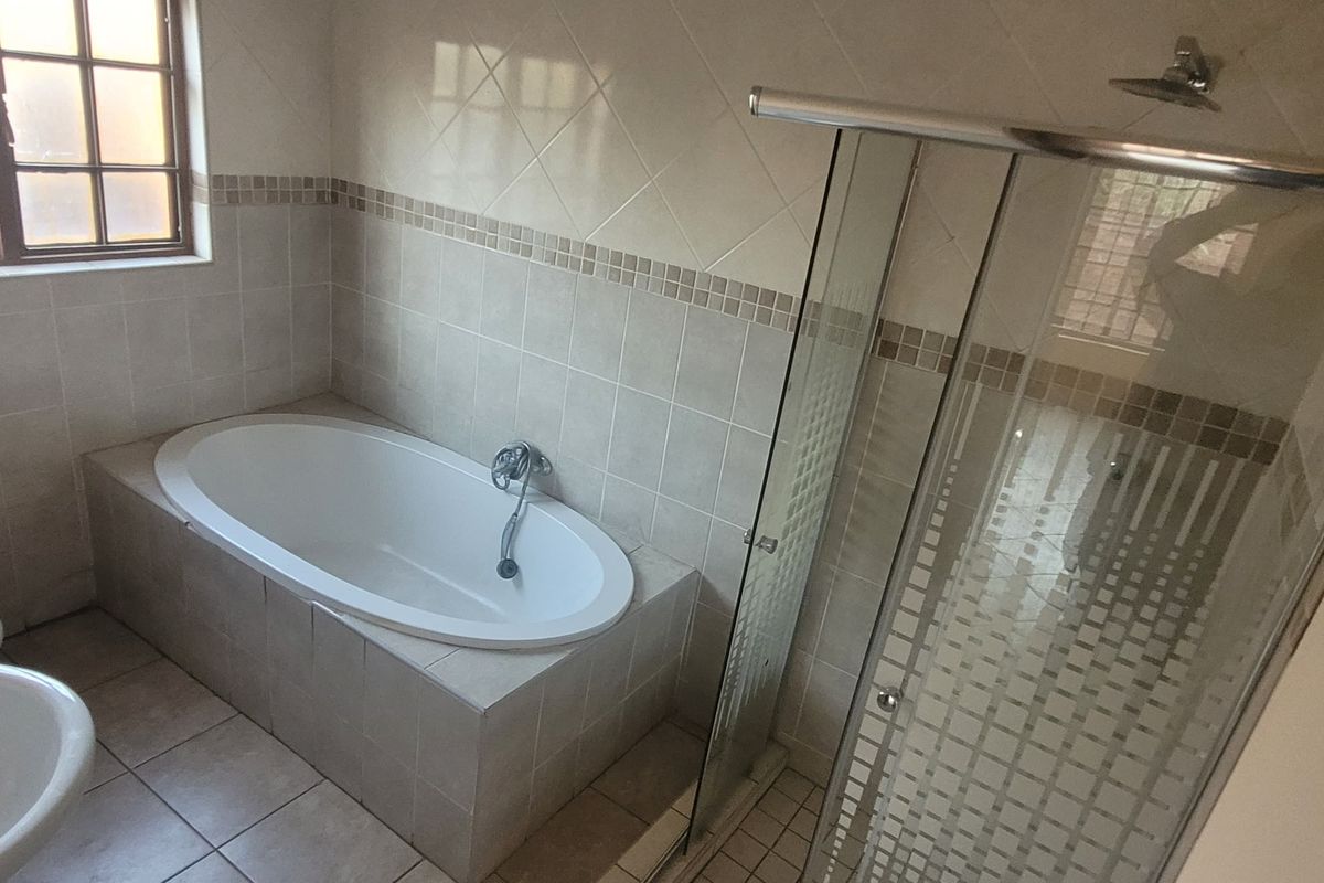 A functional bathroom featuring a built-in bathtub, a separate glass-enclosed shower, a pedestal basin, and a toilet with neutral wall and floor tiling.