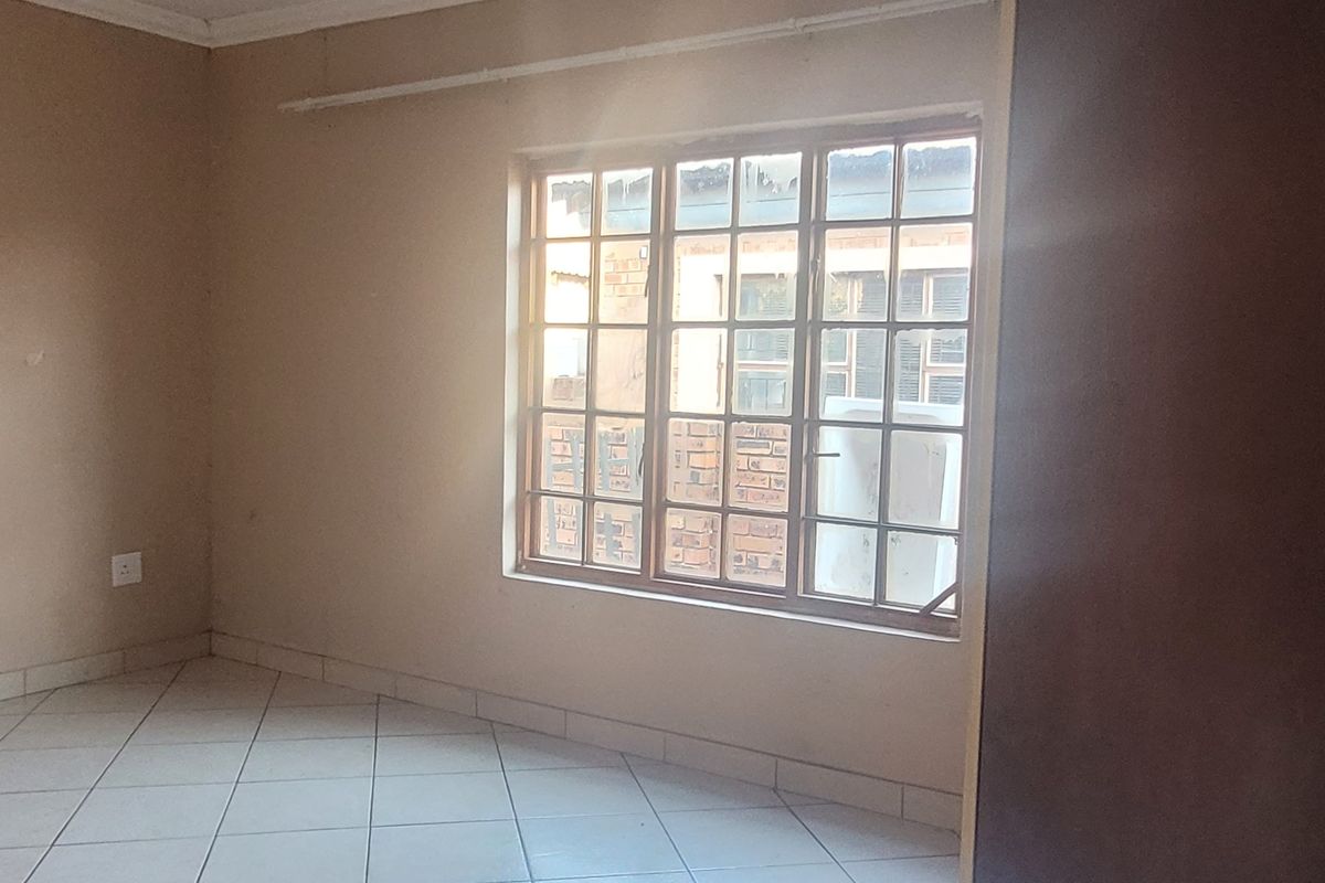 An empty bedroom featuring tiled flooring, neutral walls, and a grid-pattern window, providing a blank canvas for personalization.