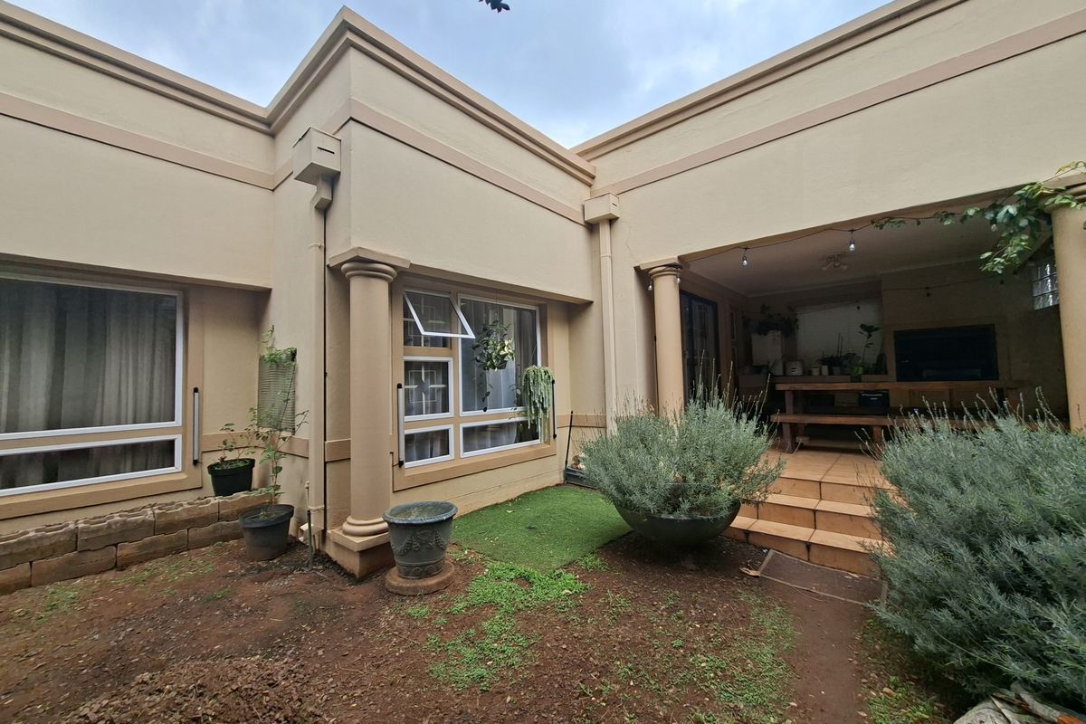 Rear view of the house featuring a covered patio with a built-in braai, decorative columns, and access to the garden area.