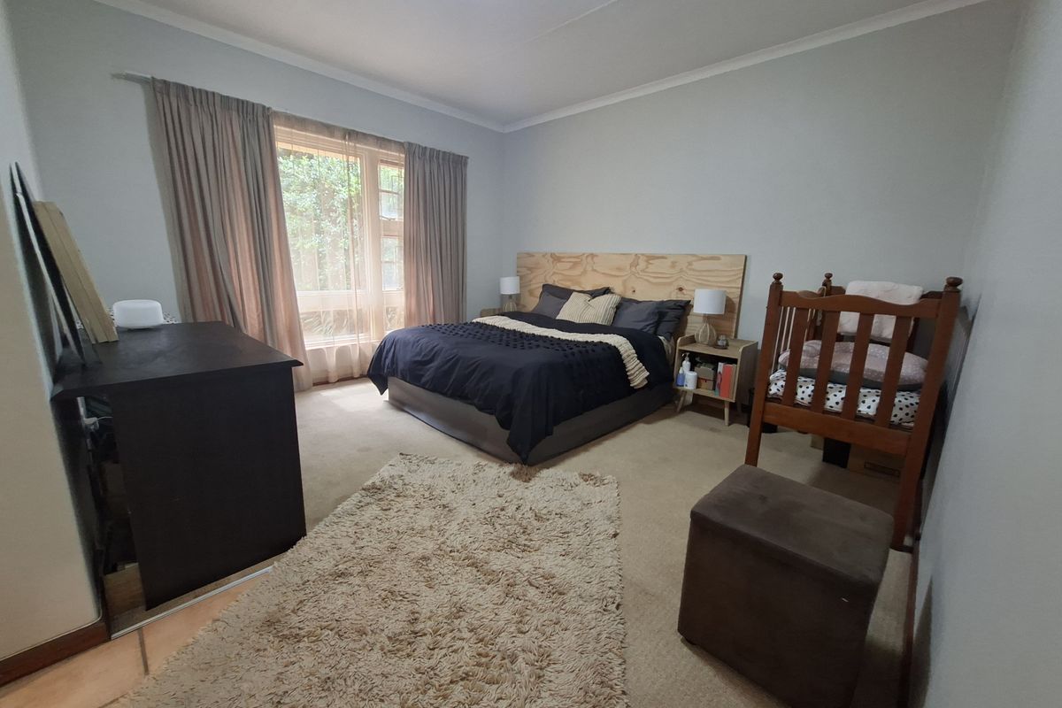 A spacious bedroom featuring neutral wall tones, carpeted flooring, and large windows with curtain tracks, offering a comfortable and functional living space.
