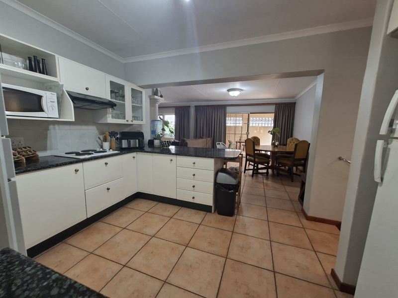Open-plan kitchen and dining area featuring white cabinetry, granite countertops, electric hob, and ceramic tiled flooring throughout the connected living space.