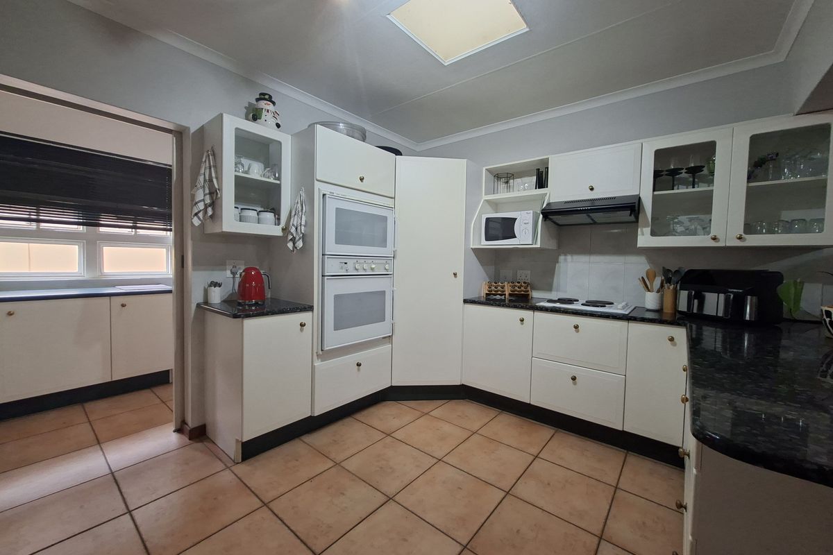 A functional kitchen featuring white cabinetry, granite countertops, a built-in double oven, hob, extractor fan, and a skylight for natural illumination.