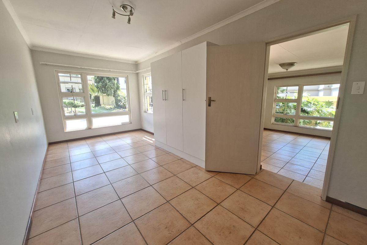 A bright, empty bedroom featuring tiled flooring, built-in cupboards, and large windows that provide ample natural light.