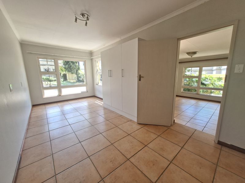 A bright, empty bedroom featuring tiled flooring, built-in cupboards, and large windows that provide ample natural light.