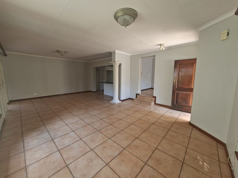 Spacious open-plan living area featuring neutral walls, tiled flooring, a decorative column, and a built-in breakfast bar, offering a versatile layout.