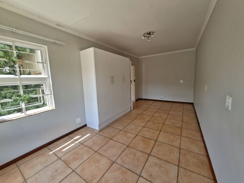 A spacious, empty bedroom featuring neutral walls, tiled flooring, and a built-in wardrobe, offering a blank canvas for personalization.