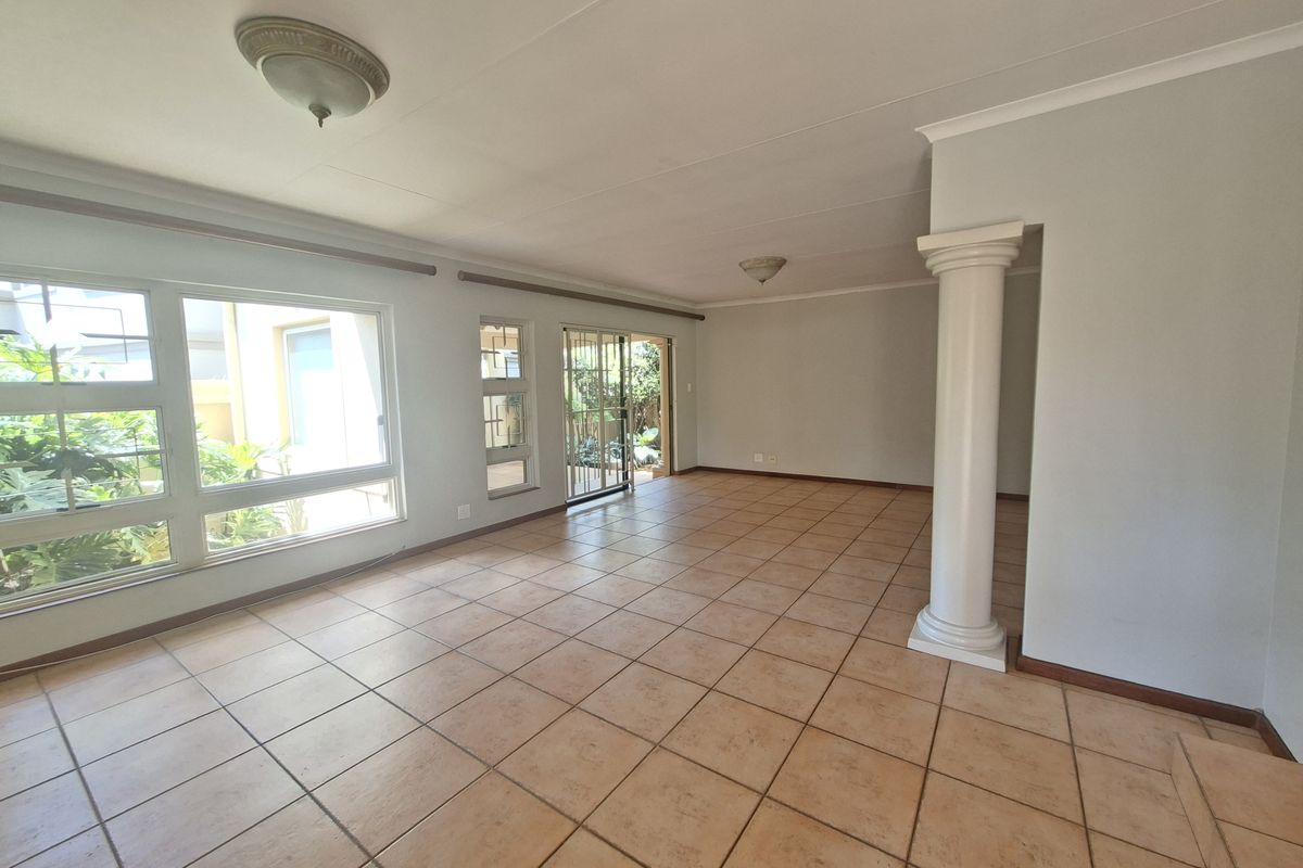 Spacious, light-filled living area featuring neutral tiled flooring, a decorative column, and large windows with direct access to the outdoor space.