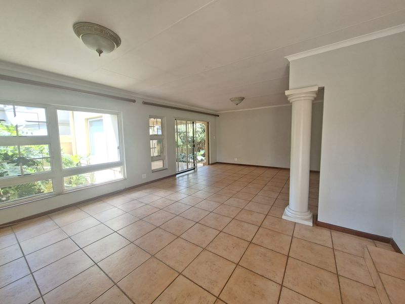 Spacious, light-filled living area featuring neutral tiled flooring, a decorative column, and large windows with direct access to the outdoor space.