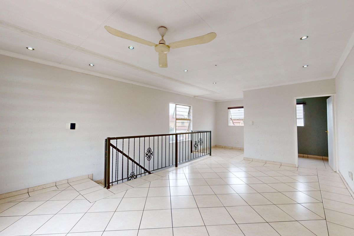 Spacious, open-plan living area featuring tiled flooring, recessed lighting, a ceiling fan, and a decorative wrought iron balustrade overlooking the staircase.