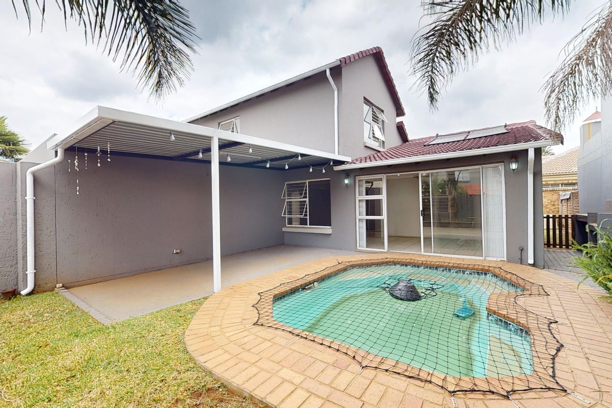 Rear exterior view featuring a swimming pool with safety net, a covered patio area, and sliding glass doors leading into the home.