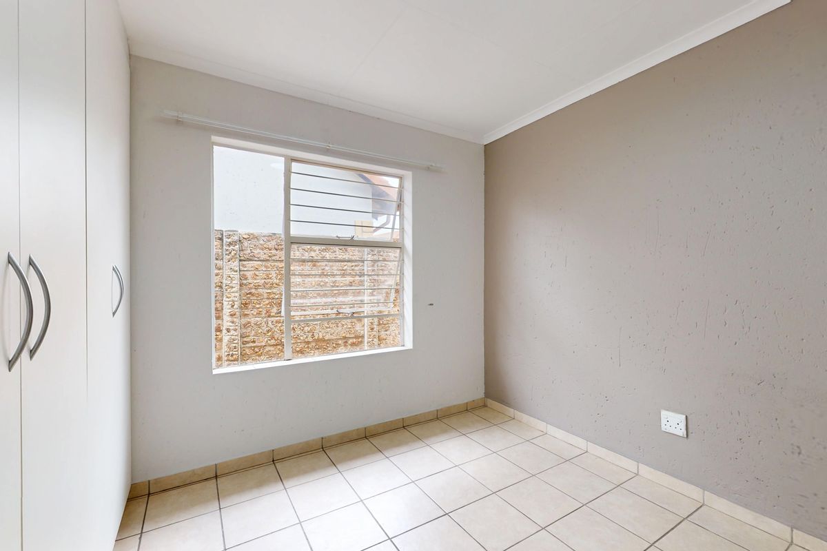 A vacant bedroom featuring tiled flooring, built-in cupboards, and a window with security bars, offering a neutral canvas for personalization.