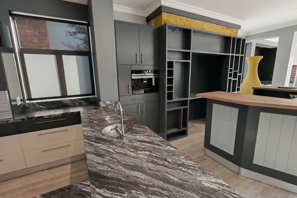 Modern kitchen featuring dark cabinetry, stone countertops, integrated coffee machine, and a breakfast bar with wood-look finish.
