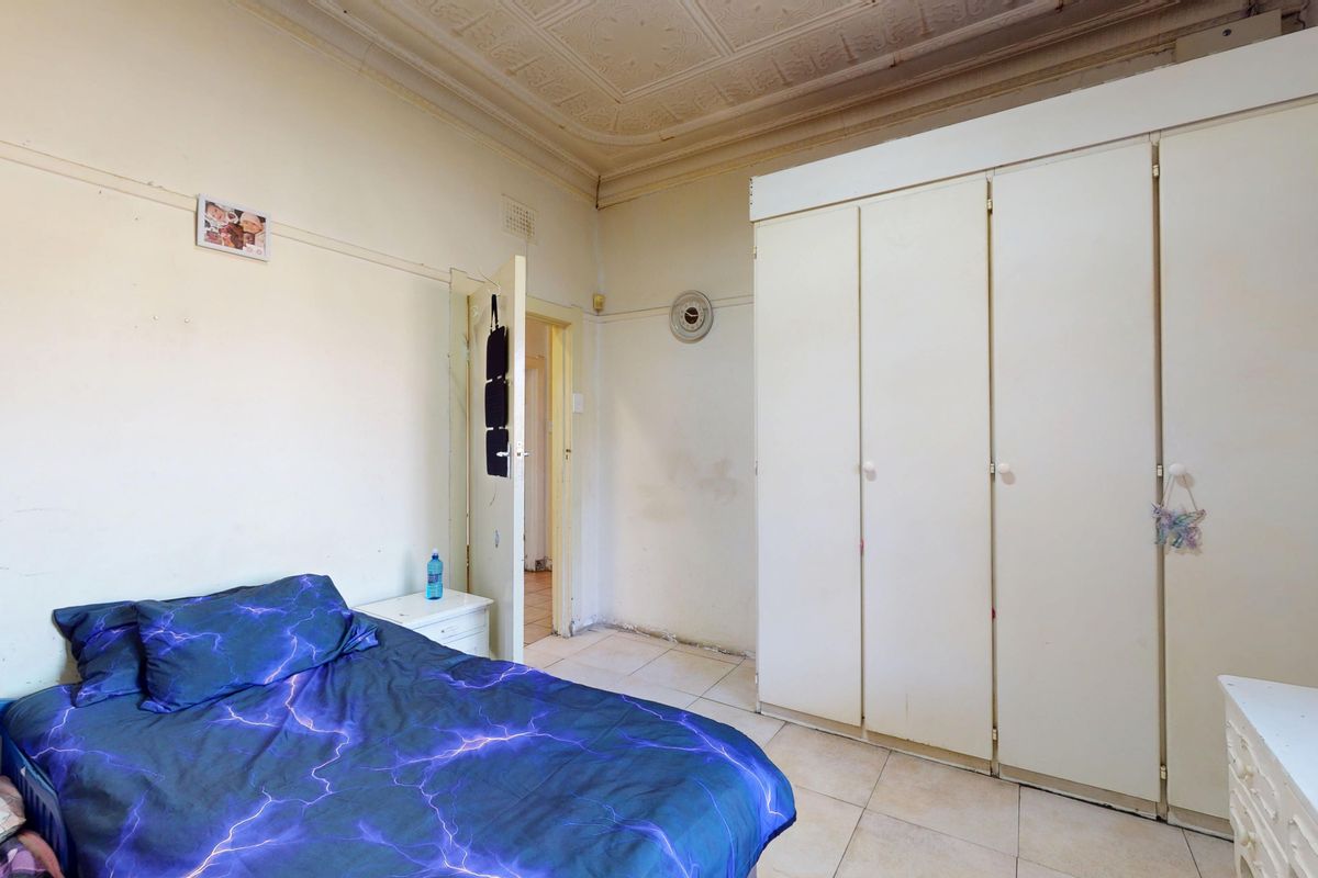A bedroom featuring built-in wardrobes, tiled flooring, and an ornate ceiling, requiring cosmetic updates to address wall and floor surface wear.