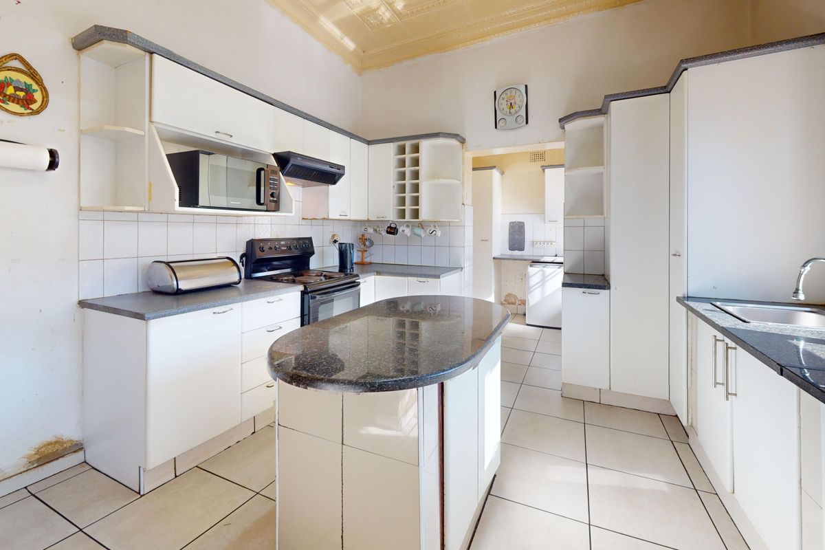 A dated kitchen featuring white cabinetry, granite countertops, a central island, and tiled flooring, offering significant potential for a modern renovation.