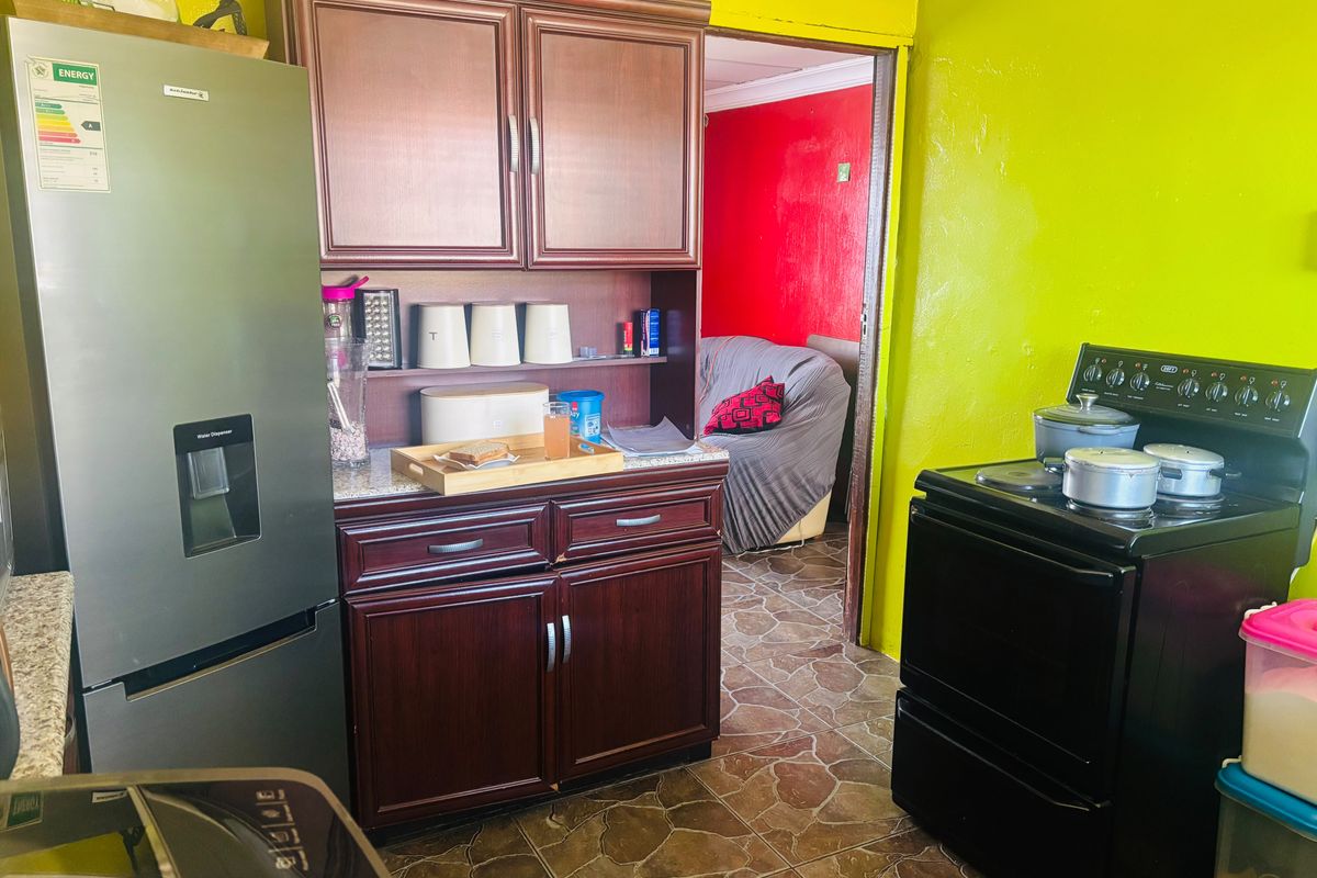 A compact kitchen featuring dark wood cabinetry, a freestanding stove, and stone-look floor tiles, with a doorway leading to an adjacent living area.