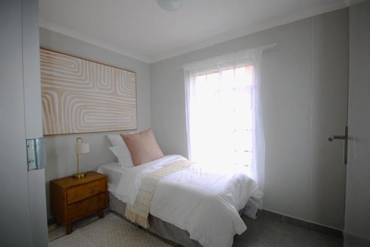 A compact bedroom featuring neutral wall tones, tiled flooring, and a window allowing natural light, suitable for a guest room or study.