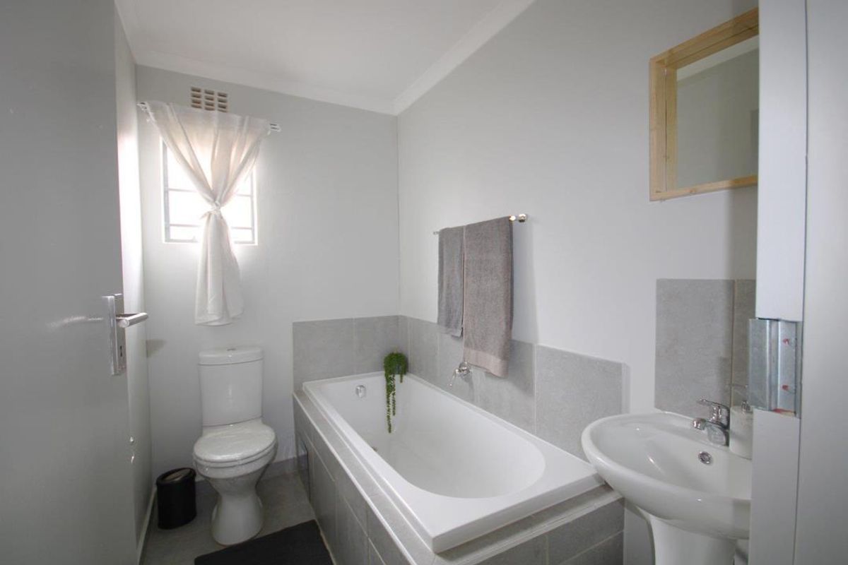 A functional bathroom featuring a built-in bathtub with tiled surround, a pedestal basin, and a standard toilet.