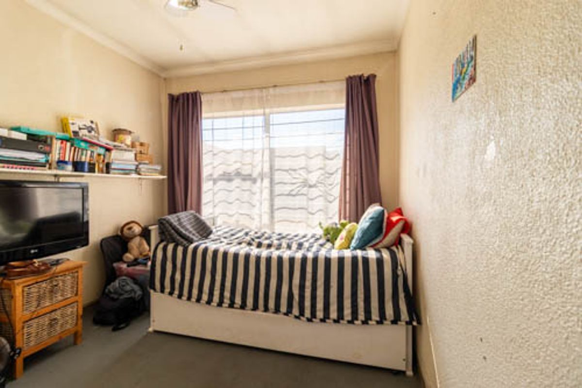 A compact bedroom featuring security bars on the window, a ceiling fan, and neutral wall finishes requiring minor maintenance.