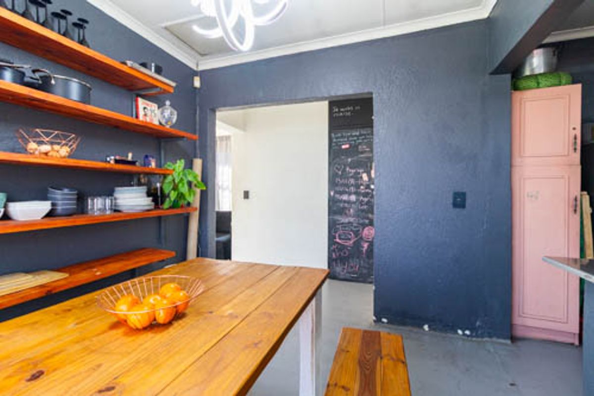 Kitchen area featuring dark painted walls, open timber shelving, a built-in pantry cupboard, and a functional chalkboard wall.