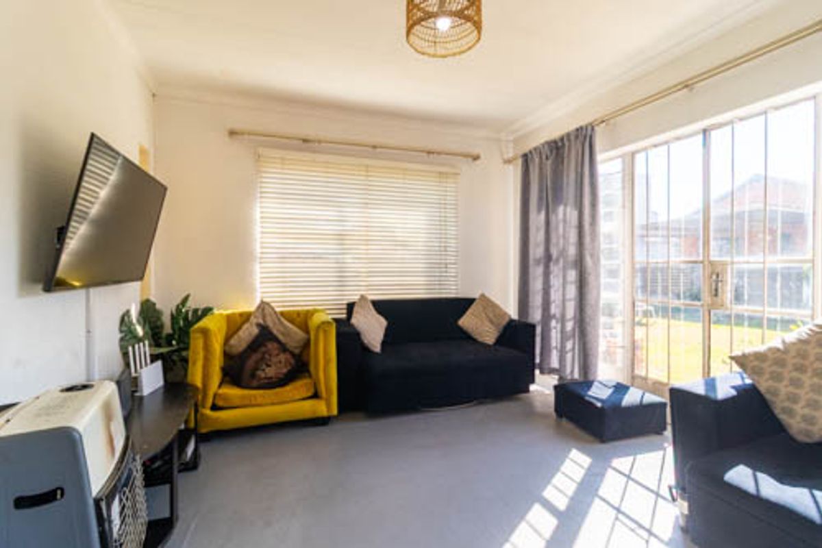 A bright living room featuring large windows with security gates, venetian blinds, and direct access to the outdoor area.