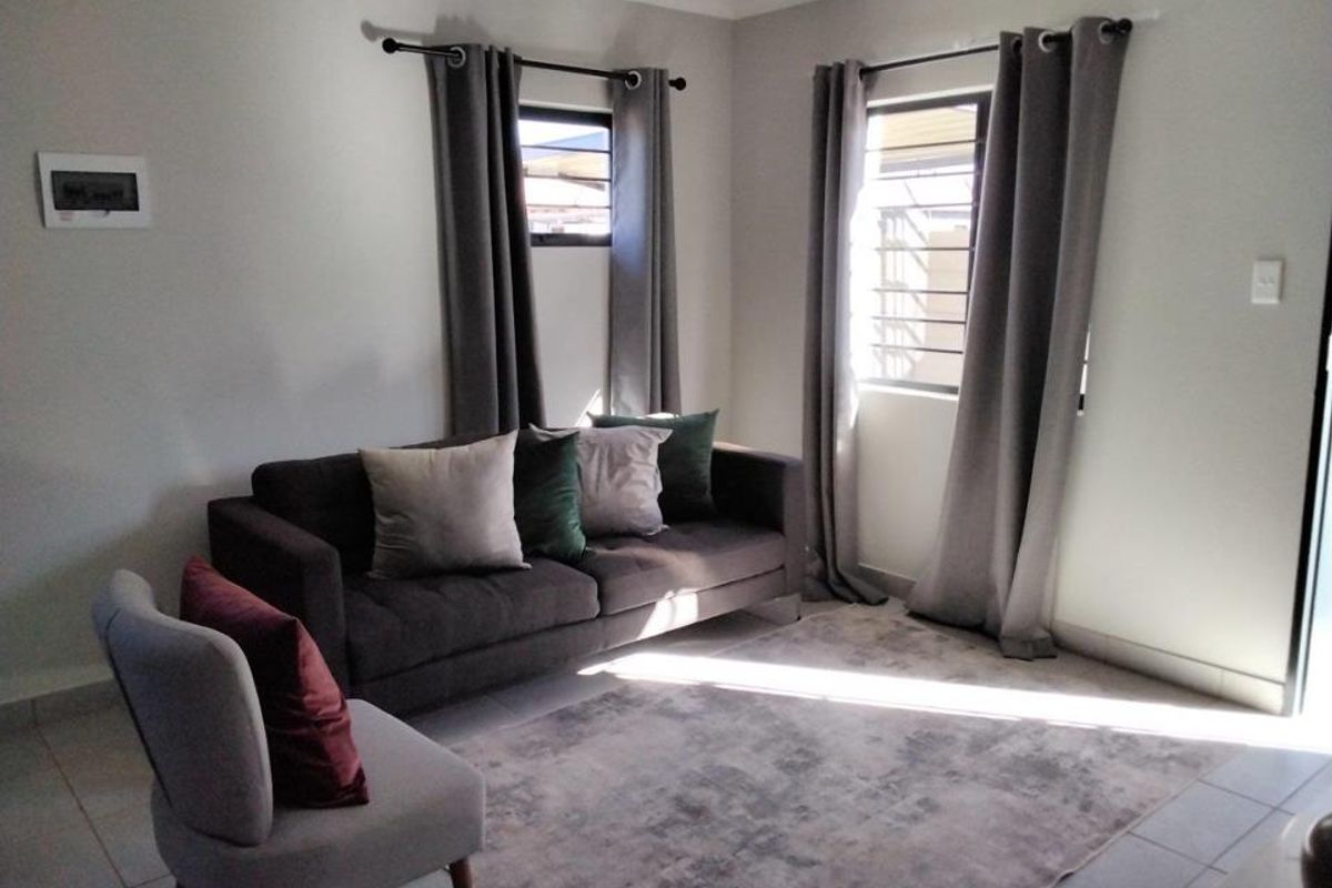 A bright living room featuring tiled flooring, neutral wall finishes, and large windows with fitted curtain rods.