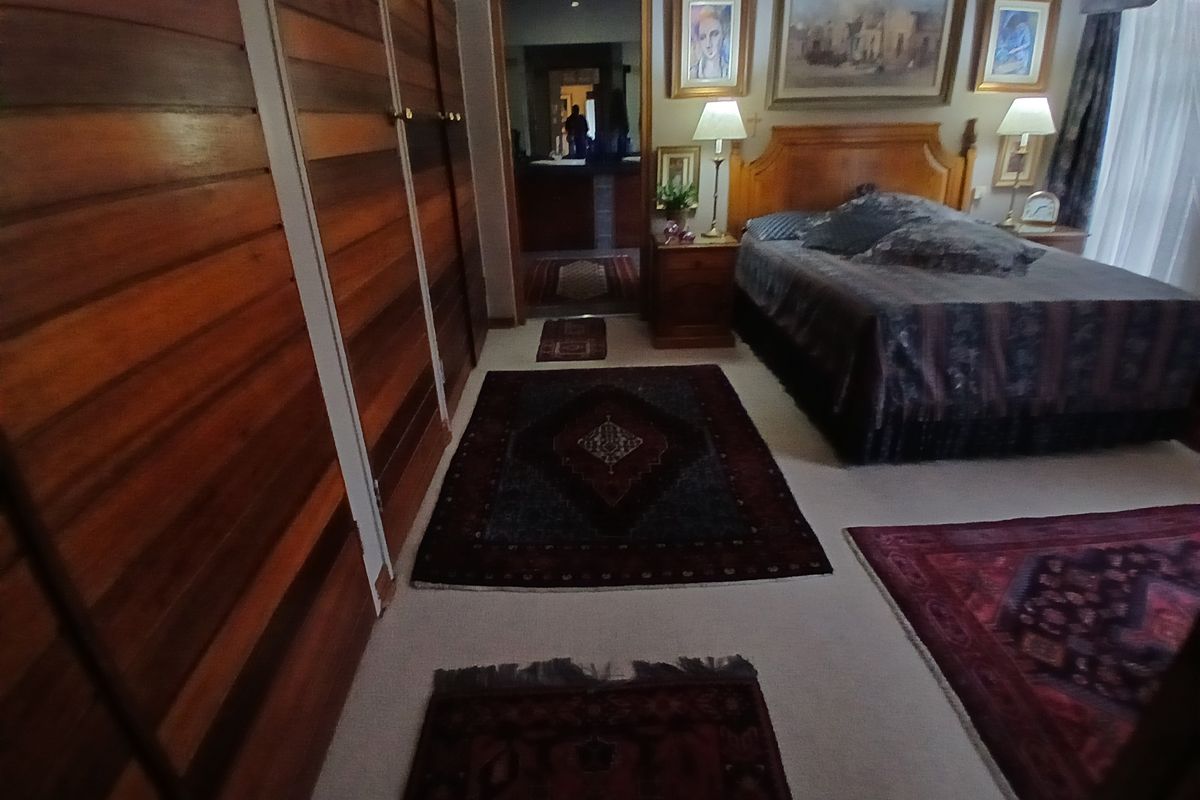 Spacious bedroom featuring extensive built-in timber panelled wardrobes and neutral carpeting, with direct access to an adjoining ensuite bathroom.