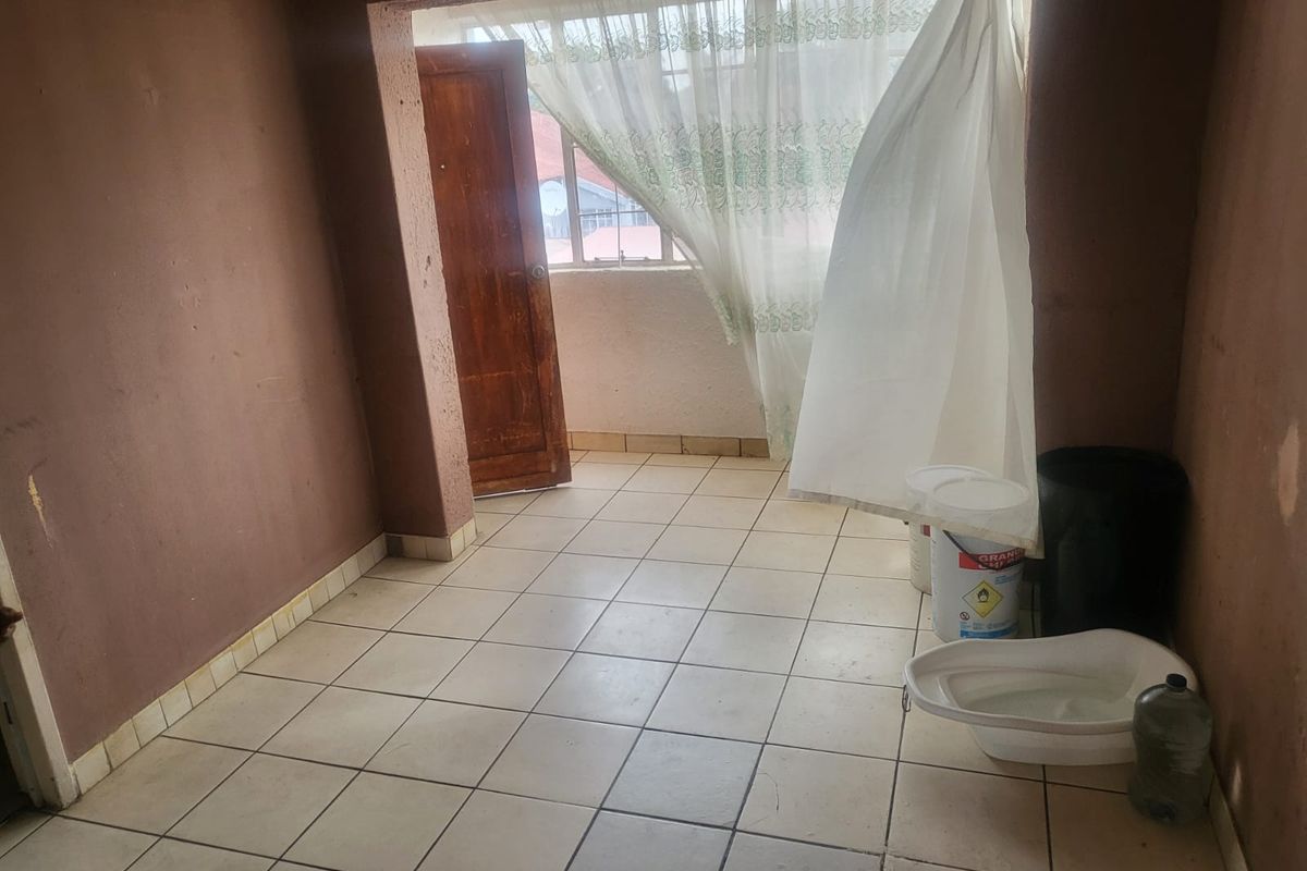 An empty living area featuring tiled flooring and a wooden door leading to an exterior space, requiring cosmetic updates to improve its condition.
