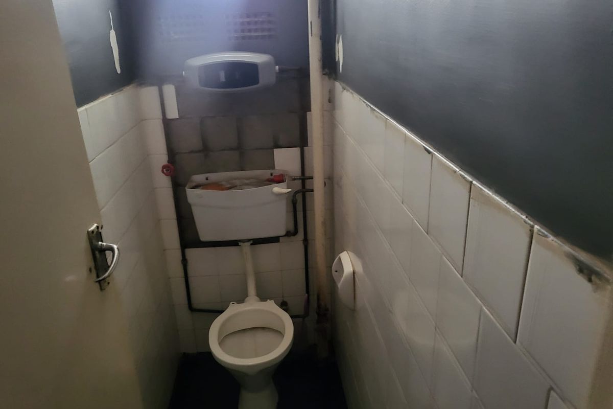 A small, dated bathroom featuring a standard toilet, exposed plumbing, and partially tiled walls requiring maintenance and cosmetic updates.