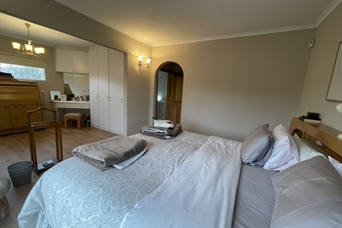 Spacious bedroom featuring built-in cupboards, laminate flooring, and a classic archway leading to an adjoining area.