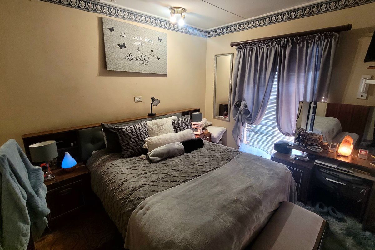 A cozy bedroom featuring a built-in headboard, decorative wallpaper border, and window treatments, offering a comfortable and functional sleeping space.