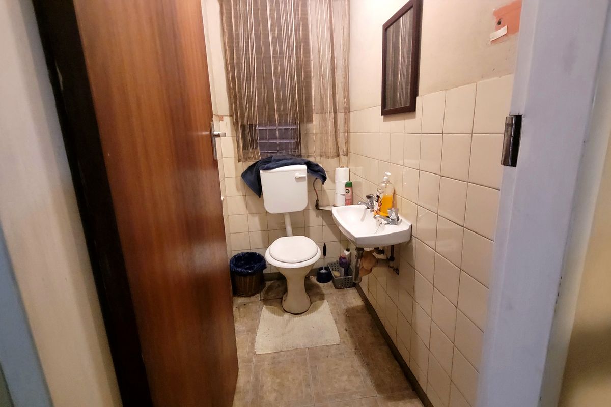 A compact bathroom featuring a wall-mounted basin and standard toilet, finished with dated wall tiling and vinyl flooring.