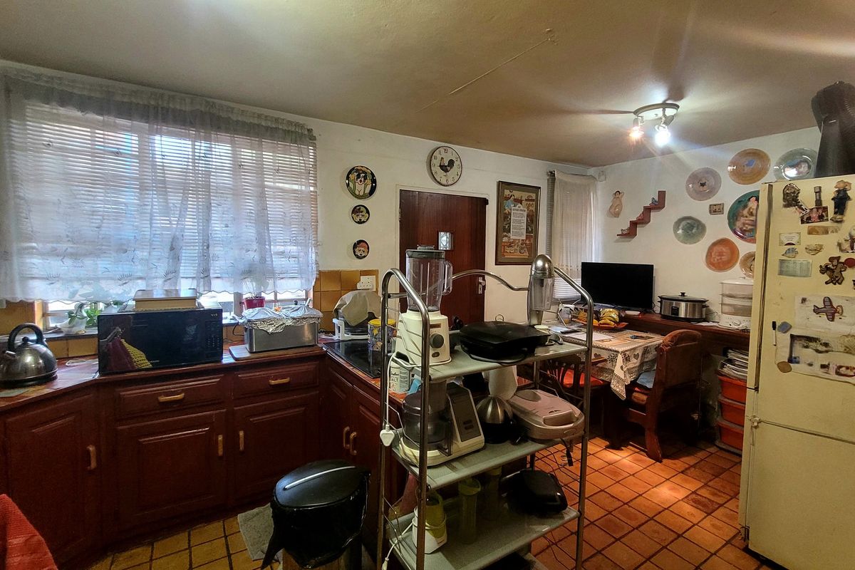 A dated kitchen featuring traditional wooden cabinetry, tiled flooring, and integrated cooking appliances, offering potential for a modern renovation.